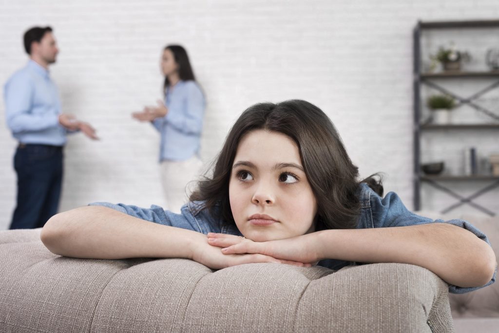 Young girl looking sad while parents argue because of their divorce